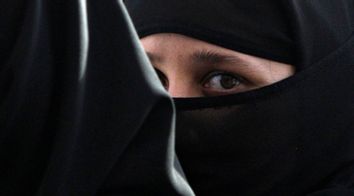 A girl wearing a burqa hides behind another as they visit the Abdullah Shah Ghazi Mausoleum in Karachi