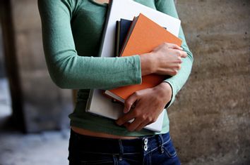 Close up of a female university student holding books and a lapt
