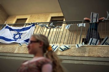 A woman walks past an Israeli flags hanging on a balcony before a ribbon-cutting ceremony at a recently built Jewish settlement in the East Jerusalem neighbourhood of Ras al-Amud May 25, 2011.