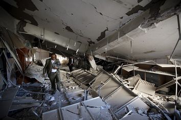 Men walk on the rubble at the Chamber of Trade and Industry headquarters after it was hit by a Saudi-led air strike in Yemen's capital Sanaa