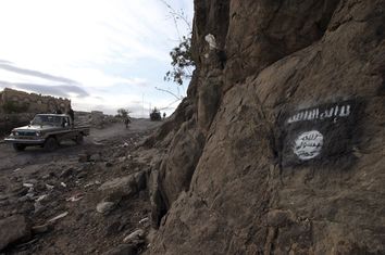 Shi'ite Houthi rebels drive a patrol truck past an Ansar al-Sharia flag painted on the side of a hill in Almnash