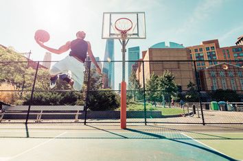 Street basketball athlete performing huge slam dunk on the court