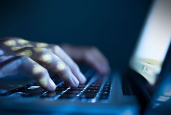 Hands typing on laptop in the dark