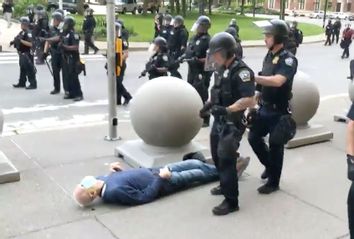 An elderly man is knocked to the ground by two police officers