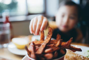 Little girl reaching for fries in a restaurant