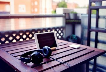 Improvised desk on the balcony, with a wooden table, a digital tablet and headphones
