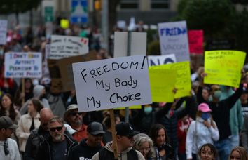 Anti-vaccine protesters hold signs, including one which reads 