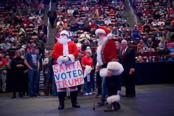 A Trump supporter in a Santa costume holds a sign that reads 