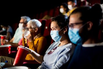 Young couple with protective face masks watching the movie at the cinema and enjoying