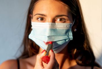 Young woman painting her lips red over a face mask