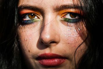  person with rainbow colored eye makeup looks on as members and supporters of the LGBTQ community