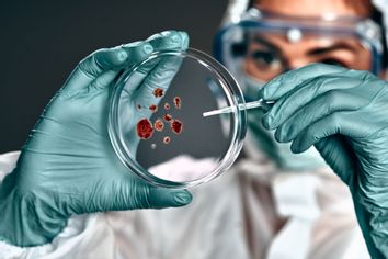 Biochemist in hazmat suit holding petri dish with biomaterial