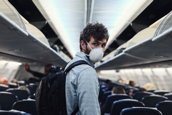 Shot of a young man wearing a mask and boarding an airplane