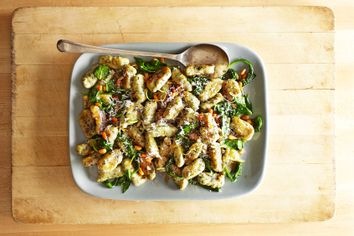 A plate with gnocchi, spinach, pine nuts and shredded cheese