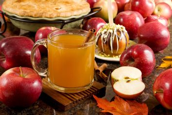 A cup of hot apple cider, caramel apple and apple pie surrounded by fresh fruits