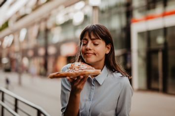 Portrait of a young woman smelling and about to taste a pizza slice.