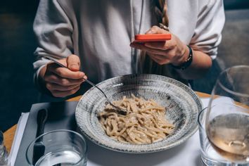 A woman takes a photo of a plate of spaghetti pasta on a smartphone in a restaurant.
