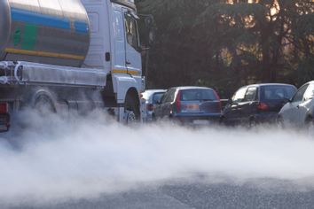 Traffic idling on forested road, plumes of exhaust funnel out into the air