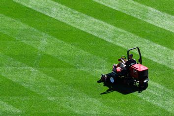 groundskeeper carefully guides the riding mower in the outfield