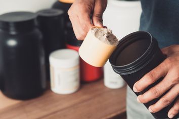 Hands holding scoop of whey protein and shaker