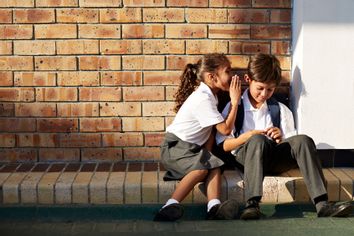 Schoolgirl whispering in classmates ear