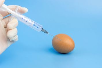 A hand in a medical glove injects a syringe into a chicken egg