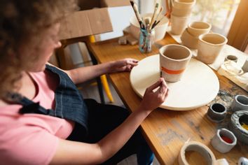 Craftswoman painting ceramic pot in her workshop