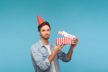 Frustrated man with party hat holding opened gift box