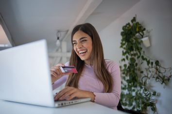 Woman happily holding credit card at computer; online shopping