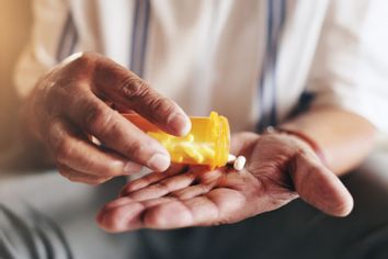 Close-up of an elderly man pouring out a pill from a medicine bottle.