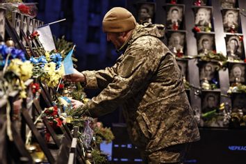Ukrainian military member puts Ukraine flag at the memorial of Heavenly Hundred Heroes