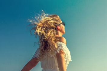 A woman walks in the sun on a windy beach.