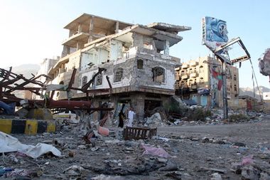 People walk past a building destroyed during recent fighting in Yemen's southwestern city of Taiz