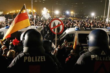 People attending an anti-immigration demonstration organised by PEGIDA walk past opponents of PEGIDA behind police cars, in Dresden