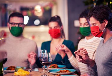 Group of friends in masks praying over Thanksgiving table at home