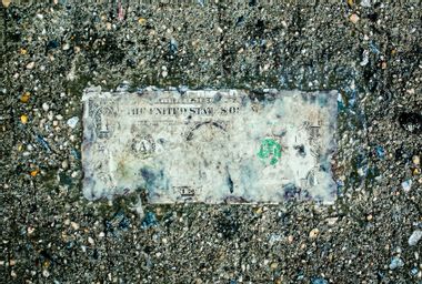 Deteriorating one dollar bill on wet pavement
