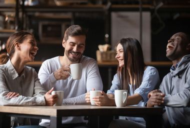 Happy friend group chatting laughing drinking coffee in cafe