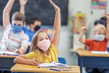 Group of students wearing protective face masks while raising their hands in class