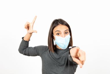 Woman making the looser sign while wearing a medical face mask