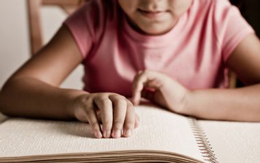 child reading braille in a book with her hands