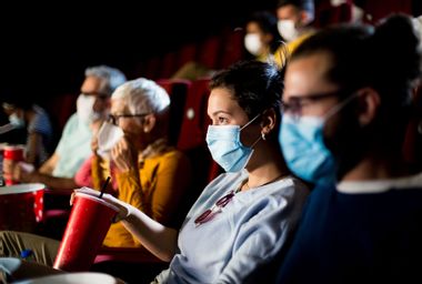 Young couple with protective face masks watching the movie at the cinema and enjoying