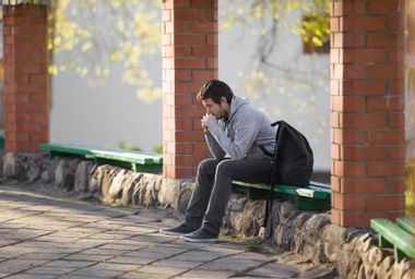 A young sad adult man sitting alone on wooden bench