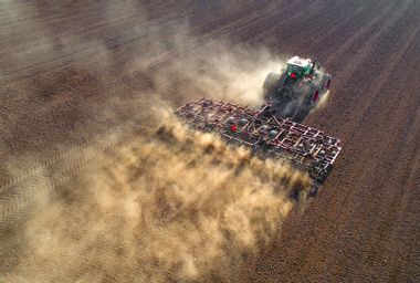 Big farm tractor tilling dusty Springtime fields