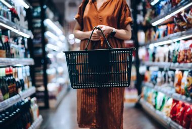 A young woman carrying a shopping basket, standing along the product aisle