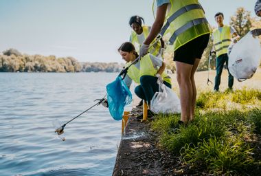 Young female and male environmentalist cleaning lake while picking plastic from claw