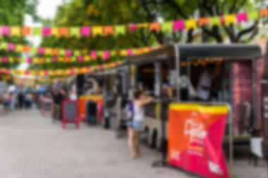 Food trucks and people at a street food market festival on a sunny day, blurred