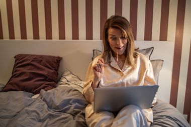 Mature woman lying in bed and looking at her laptop