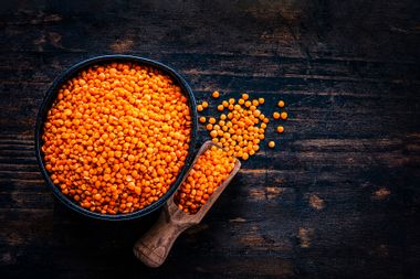Red lentils in a black bowl shot from above on dark wooden table