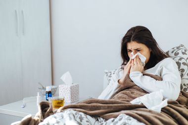 Sick Woman Lying In Bed With Tissues
