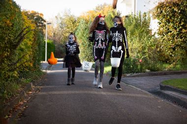 Child and teenagers walking along a narrow urban street whilst out trick or treating for Halloween